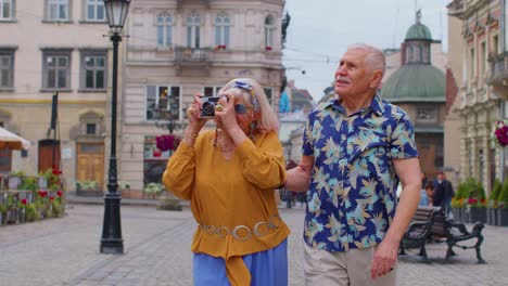 Senior-old-stylish-tourists-man-woman-walking,-taking-photos-on-old-camera-at-summer-city-center