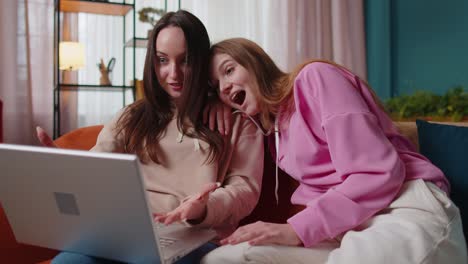 Young-adult-women-couple-looking-at-laptop-notebook-screen-making-online-shopping-purchase-at-home