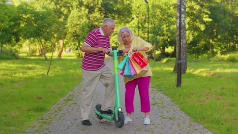 Elderly-stylish-couple-grandmother,-grandfather-after-shopping-with-bags-using-scooter-for-riding