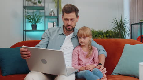 Child-kid-daughter-having-fun-with-father-or-nanny-enjoying-using-laptop-pc-watch-cartoons-at-home