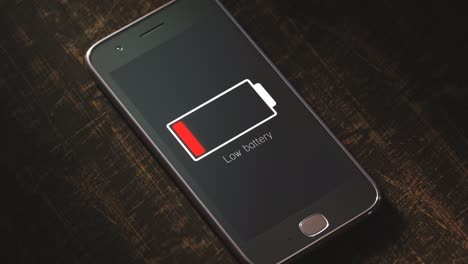 Smartphone-screen-showing-notification-about-low-battery-status.-A-warning-message-with-flashing-battery-symbol-about-low-battery-power-or-exhaustion.-Close-up-of-generic-smartphone-on-wooden-desk.