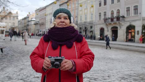 Senior-woman-tourist-taking-pictures-with-photo-camera,-using-retro-device-in-winter-city,-lockdown