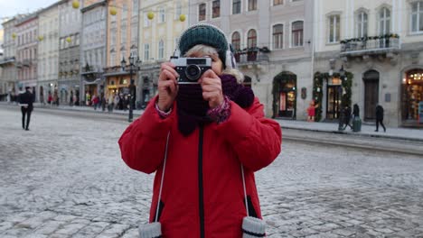 Senior-woman-tourist-taking-pictures-with-photo-camera,-using-retro-device-in-winter-city-center
