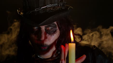 Frightening-creepy-senior-woman-with-Halloween-witch-makeup-looking-at-candle,-conjure,-hex,-wiz