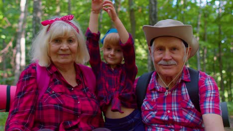 Old-senior-grandparents-couple-tourists-hikers-resting-in-forest-with-granddaughter-in-summer-wood