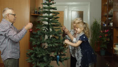 Niña-Con-Abuela-Y-Abuelo-Decorando-Un-árbol-De-Navidad-Artificial-Con-Juguetes.