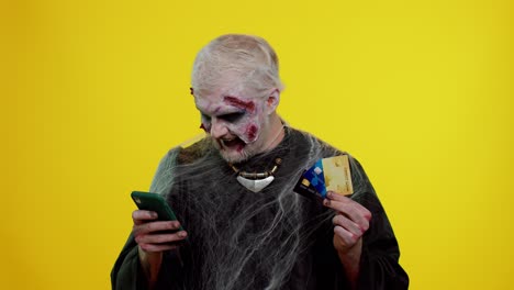 Sinister-man-Halloween-zombie-using-credit-bank-cards-and-smartphone-while-purchases-online-shopping