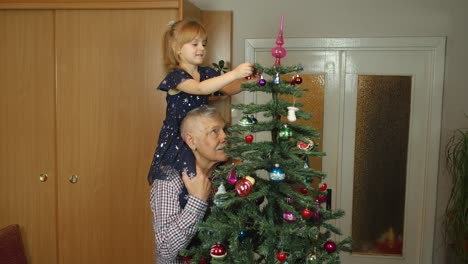 Children-girl-with-elderly-grandparent-decorating-artificial-Christmas-pine-tree-at-old-fashion-home