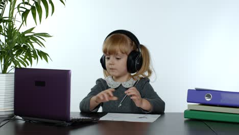 Teen-girl-school-student-wearing-wireless-headphones-calling-teacher-on-laptop.-Distance-education