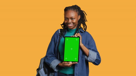 Smiling-woman-presenting-tablet-with-green-screen-display,-studio-background