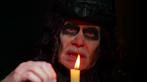 Frightening-creepy-senior-man-with-Halloween-witcher-makeup-looking-at-candle,-conjure,-hex,-wiz