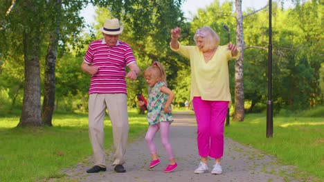 Granddaughter-together-with-senior-grandmother-grandfather-listening-to-music,-dancing-crazy-in-park