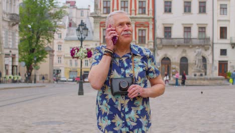 Älterer-Alter-Tourist-In-Stilvoller-Kleidung,-Der-Beim-Spazierengehen-Auf-Der-Stadtstraße-Mit-Dem-Mobiltelefon-Telefoniert