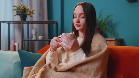 Portrait-of-smiling-young-adult-woman-in-warm-white-sweater-drink-hot-beverage-mug-relaxing-at-home