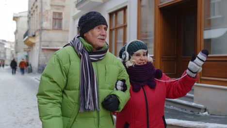 Senior-old-couple-grandmother-and-grandfather-in-colorful-winter-jackets-walking-in-winter-city