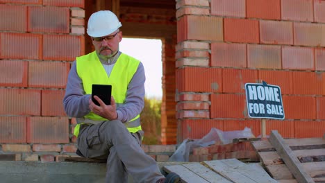 Architect-man-with-digital-tablet-computer-at-construction-site,-analyzing-blueprints-building-house
