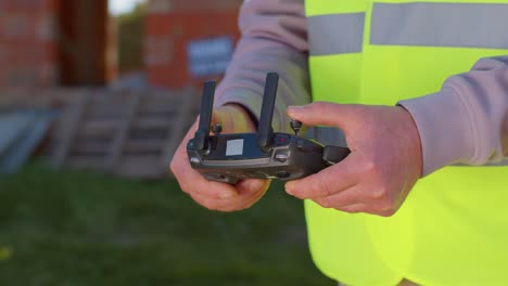 Drone-operator-holding-remote-controller-controls-an-aircraft-in-front-of-construction-house-site