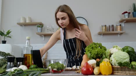 Vegan-woman-looking-for-culinary-recipe-online-on-digital-tablet.-Cooking-salad-with-raw-vegetables
