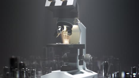 Modern-microscope-standing-in-a-foggy,-moody-laboratory.-Light-rays-pouring-through-a-dense-fog.-Scientific-equipment-lit-by-bright-spotlight.-Camera-heading.-Countless-glassware-pieces-on-a-floor.
