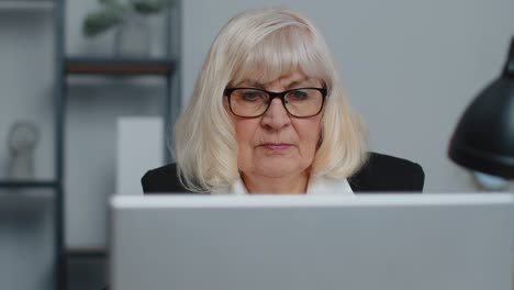 Una-Mujer-De-Negocios-Senior-Usa-Gafas-Trabajando-En-La-Oficina-Del-Hogar,-Seminario-Web-En-Línea-Usando-Una-Computadora-Portátil