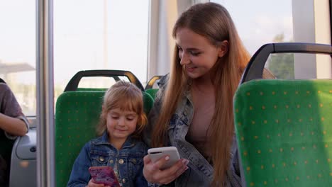 Mother-with-daughter-traveling-by-bus-going-home,-playing-on-smartphone,-browsing-social-media