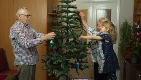 Kleines-Süßes-Mädchen-Mit-Der-Familie-Der-älteren-Großeltern,-Die-Zu-Hause-Einen-Künstlichen-Weihnachtsbaum-Schmücken