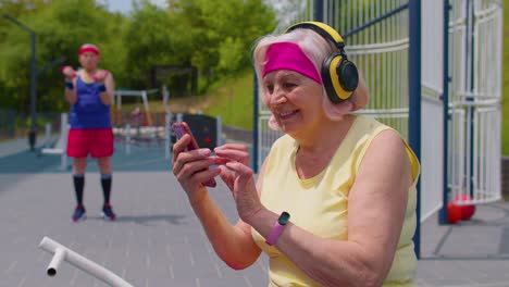 Senior-old-sportsman-grandfather-with-headphones-listening-music-from-mobile-phone-on-playground