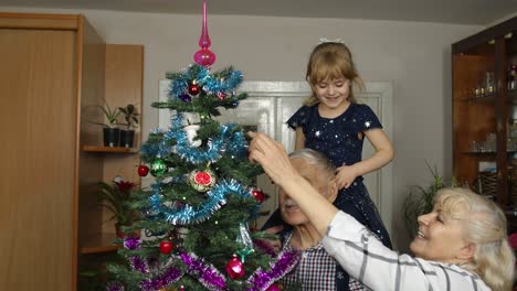 Kleines-Mädchen-Mit-Großmutter-Und-Großvater,-Die-Einen-Künstlichen-Weihnachtsbaum-Mit-Spielzeug-Dekorieren