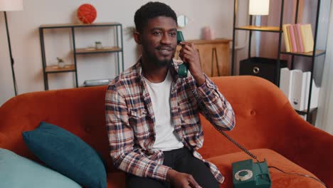Young-adult-african-american-man-enjoying-talking-on-retro-phone-conversation-with-friends-at-home