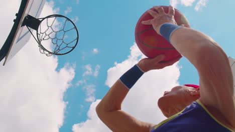 Upward-view-of-senior-sportsman-guy-grandfather-trains-throwing-ball-into-basketball-hit-ring-basket