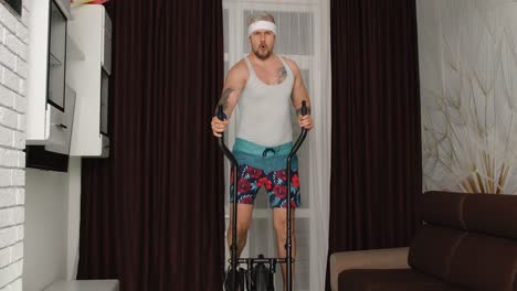 Sportsman-retro-guy-in-funny-clothes-making-sport-workout-fitness-cardio-exercises-on-orbitrek-home