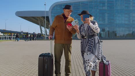 Senior-rich-pensioner-tourists-grandmother-grandfather-stay-near-airport-hall-hold-money-dollar-cash