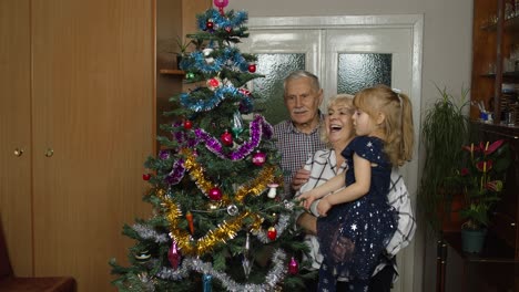 Kid-with-senior-grandmother-and-grandfather-decorating-artificial-Christmas-tree,-lights-garlands
