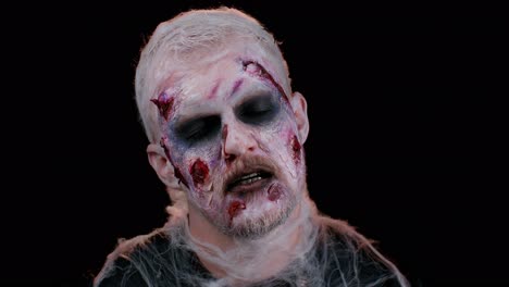 Zombie-man-with-makeup-with-fake-wounds-scars-looking-at-camera-and-screaming,-trying-to-scare