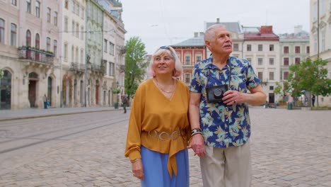 Senior-stylish-couple-tourists-man,-woman,-grandmother,-grandfather-walking-along-street-in-old-town