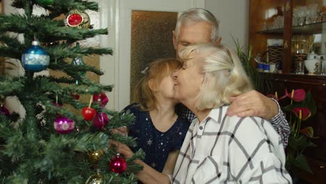 Una-Niña-Pequeña-Y-Linda-Con-Una-Familia-De-Abuelos-Mayores-Decorando-Un-árbol-De-Navidad-Artificial-En-Casa