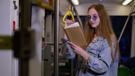 Portrait-of-attractive-young-adult-woman-stay-at-empty-subway-train-and-reading-interesting-book