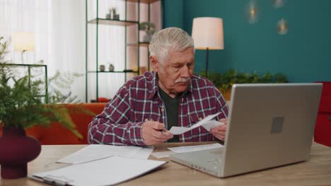 Serious-grandfather-man-calculating-household-bills-bank-loan-online-domestic-expenditures-payment