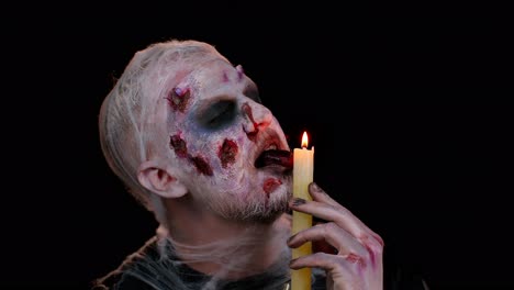 Man-with-Halloween-zombie-bloody-wounded-makeup,-trying-to-scare,-spells-conjures-over-a-candle