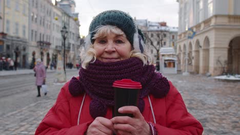 Portrait-of-senior-woman-tourist-smiling,-looking-at-camera-in-winter-city-center-of-Lviv,-Ukraine