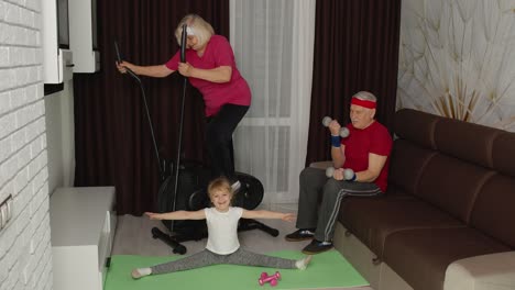 Senior-couple-with-granddaughter-using-orbitrek,-doing-weight-lifting-dumbbells-exercises-at-home