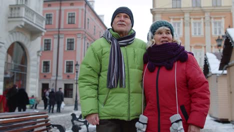 Senior-old-couple-tourists-man-woman-walking,-talking,-gesturing-in-winter-snowy-city-Lviv,-Ukraine