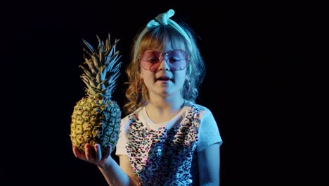 Stylish-teen-caucasian-kid-girl-with-pineapple-standing-on-black-background-singing,-fooling-around