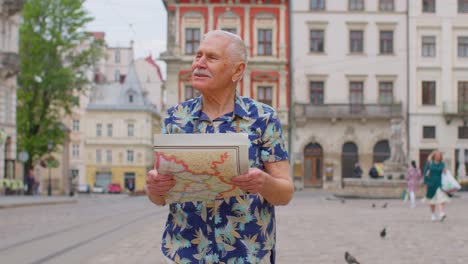 Senior-stylish-tourist-grandfather-man-walking-along-street-looking-for-way-using-paper-map-in-city