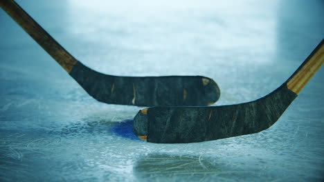 Two-ice-hockey-sticks-fighting-for-a-puck-on-a-scratched-ice-rink-surface.-Two-players-struggle-in-contact-sport-match-using-the-sticks-to-shoot-puck-into-net-to-score-points.-Slow-motion-close-up