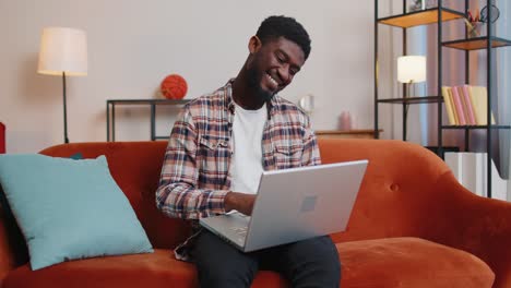 Afroamerikanischer-Junger-Mann,-Der-Auf-Dem-Sofa-Sitzt-Und-Den-Laptop-PC-Schließt,-Nachdem-Er-Online-Im-Wohnzimmer-Gearbeitet-Hat