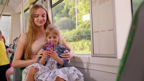 Child-girl-with-mother-using-mobile-phone-internet-social-network-application-while-traveling-by-bus