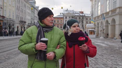 Senior-wife-husband-tourists-drinking-from-cups,-enjoying-hot-drink-tea-on-city-central-street