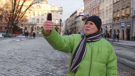 Senior-man-tourist-taking-selfie,-making-online-video-call-with-smart-phone-in-winter-city-center