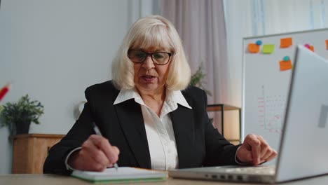Senior-elderly-business-office-woman-elearning-online-writing-notes-from-laptop,-live-webinar-online